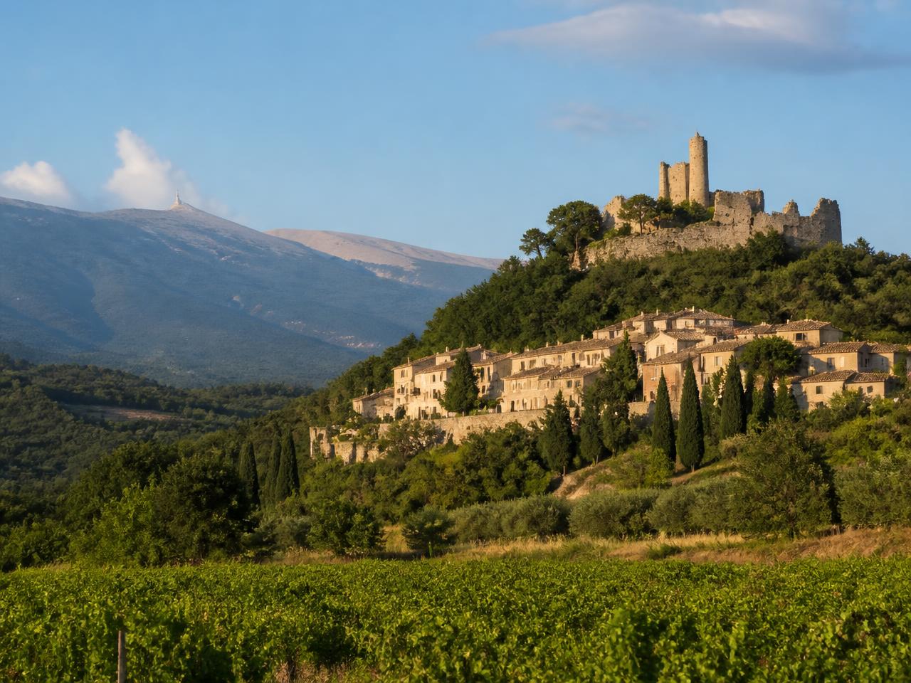 Le village d'Entrechaux dominé par les ruines de son château, entouré de vignes, avec le Mont Ventoux en arrière-plan